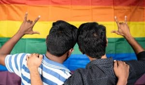 Image of a male couple in front of a rainbow flag holding up the ASL love sign. Have you been looking for a 